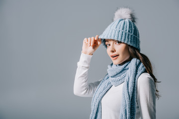 beautiful smiling girl posing in knitted hat and scarf, isolated on grey