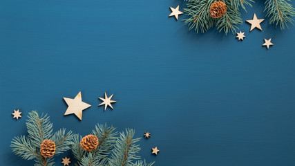 Flat lay Christmas tree branches with cones and wooden vintage stars over blue background. Top...
