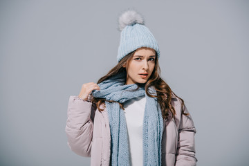 stylish girl posing in warm coat, knitted hat and scarf, isolated on grey