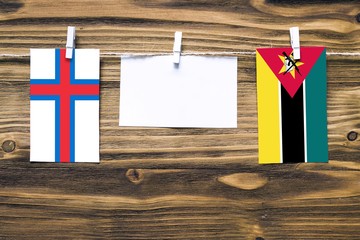 Hanging flags of Faroe Islands and Mozambique attached to rope with clothes pins with copy space on white note paper on wooden background.Diplomatic relations between countries.