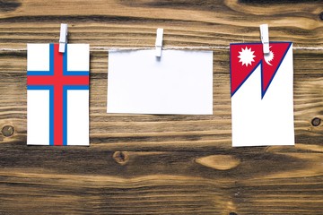 Hanging flags of Faroe Islands and Nepal attached to rope with clothes pins with copy space on white note paper on wooden background.Diplomatic relations between countries.