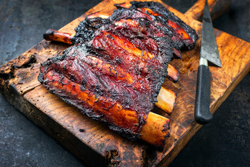 Barbecue burnt chuck beef ribs marinated with hot chili sauce as closeup on an old rustic wooden cutting board