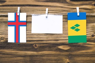 Hanging flags of Faroe Islands and Saint Vincent And The Grenadines attached to rope with clothes pins with copy space on white note paper on wooden background.Diplomatic relations between countries.