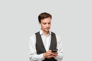 Young businessman in a white shirt and grey vest looking at the screen of a smartphone.