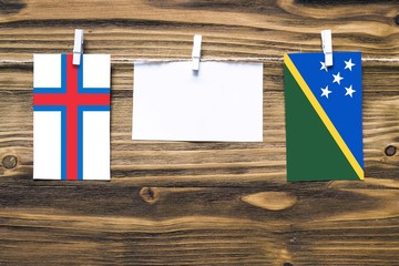 Hanging flags of Faroe Islands and Solomon Islands attached to rope with clothes pins with copy...