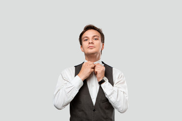 Young businessman in a white shirt and grey vest adjusting hand watches looking at the camera.