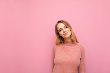 Obraz premium Portrait of attractive girl in warm sweater isolated on pink background, looking into camera and smiling. Cute lady posing on background, wearing pink sweater, isolated.