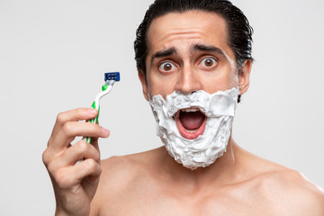 Handsome man with mustache uses shaving stick and shaving foam to trim his beard standning bare...