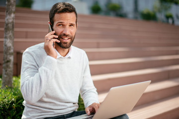 Young businessman outdoors using phone and laptop