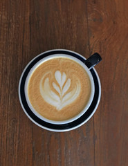 Hot milk coffee served in black cup with flower latte art and wooded table background