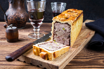 Traditional French Pate en croute with goose meat and liver as closeup with red wine on a wooden...