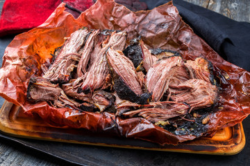 Traditional barbecue wagyu pulled beef in peach paper as closeup on a rustic board