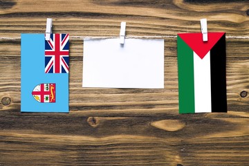 Hanging flags of Fiji and Palestine attached to rope with clothes pins with copy space on white note paper on wooden background.Diplomatic relations between countries.