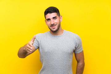 Young handsome man over isolated yellow background handshaking after good deal