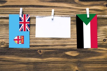 Hanging flags of Fiji and Sudan attached to rope with clothes pins with copy space on white note paper on wooden background.Diplomatic relations between countries.