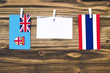 Hanging flags of Fiji and Thailand attached to rope with clothes pins with copy space on white note paper on wooden background.Diplomatic relations between countries.