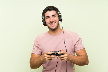 Young handsome man playing with a video game controller over isolated green wall © luismolinero