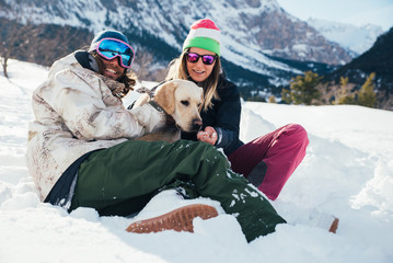 couple playing with dog on the mountains, on the snowy ground