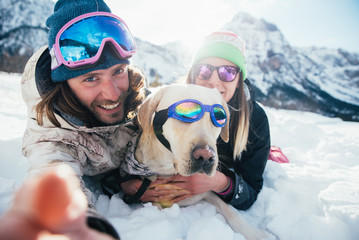 couple playing with dog on the mountains, on the snowy ground