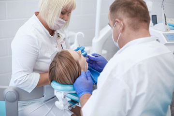 Naklejka na ściany i meble Doctor dentist treats teeth of a beautiful young girl patient. The girl on reception at the dentist. Doctor dentist treats tooth