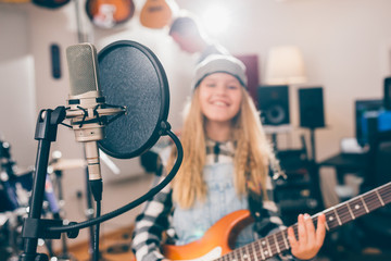 close up of studio microphone and blurred kid playing guitar in background