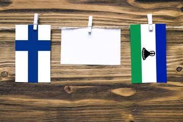 Hanging flags of Finland and Lesotho attached to rope with clothes pins with copy space on white...