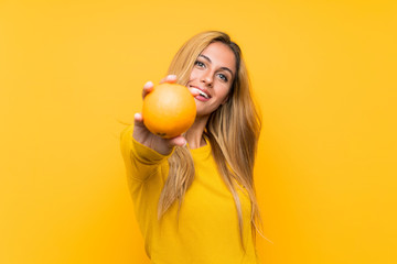 Young blonde woman holding an orange over yellow background