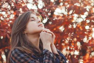 portrait of a young woman praying in nature, the girl thanks God with her hands folded at her chin,...