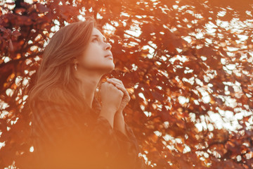 portrait of a young woman praying in nature, the girl thanks God with her hands folded at her chin,...