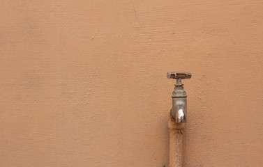 Stainless steel water tap attached to wall in building exterior.