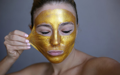 Beautiful girl peeling off golden face mask. Skin treatment.
