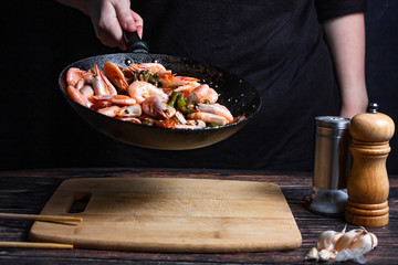 Chef at work. Hand holds a hot pan with fried shrimp and vegetables in sweet and sour sauce.