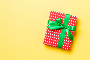 wrapped Christmas or other holiday handmade present in paper with green ribbon on yellow background. Present box, decoration of gift on colored table, top view with copy space