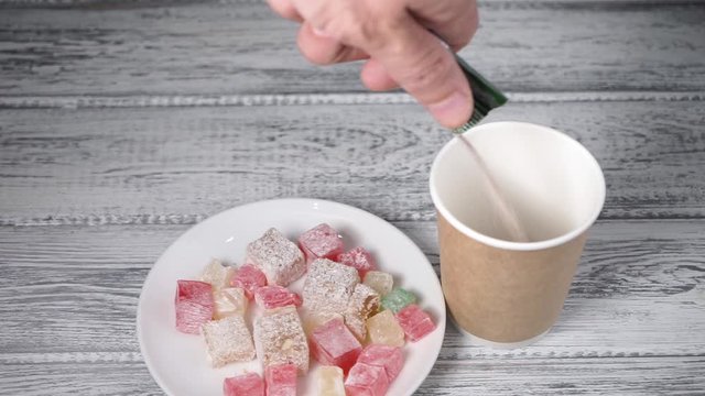 Package of coffee 3 in 1 poured into a disposable Cup. Instant coffee falling into gray mug. Light wooden table with candy