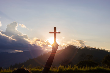 human hands praying to the GOD while holding a crucifix symbol with bright sunbeam on the sky