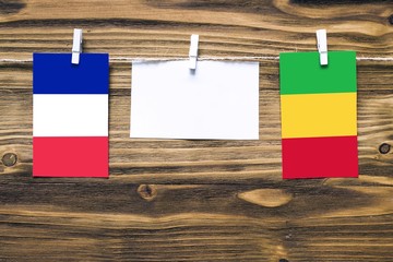 Hanging flags of France and Mali attached to rope with clothes pins with copy space on white note paper on wooden background.Diplomatic relations between countries.