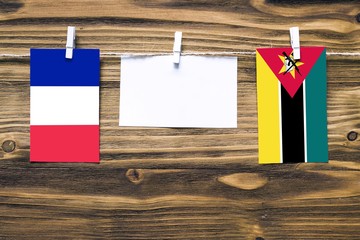 Hanging flags of France and Mozambique attached to rope with clothes pins with copy space on white...