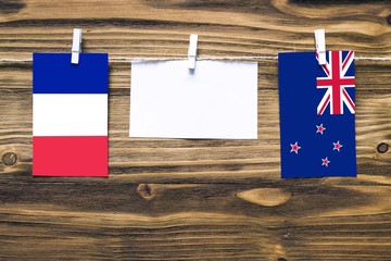 Hanging flags of France and New Zealand attached to rope with clothes pins with copy space on white note paper on wooden background.Diplomatic relations between countries.