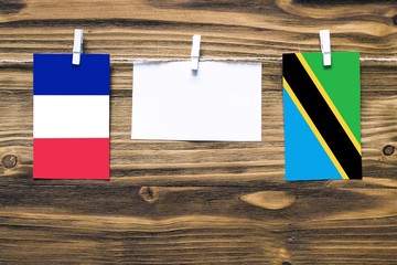 Hanging flags of France and Tanzania attached to rope with clothes pins with copy space on white...