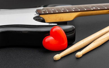 Red heart with guitar and drumsticks on black. Love music.