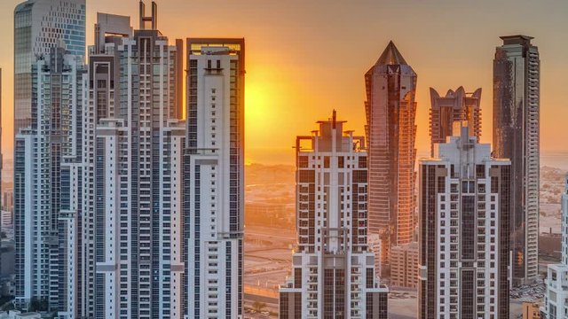 Modern residential and office complex with many towers aerial timelapse with sunset at Business Bay, Dubai, UAE. Sun behind skyscrapers moves down