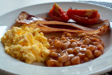 English breakfast with grilled bacon, tomatoes, scrambled eggs and baked beans in tomato sauce