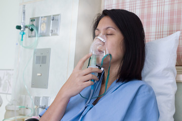 Sick beautiful female in blue cloth hold nasal mask with respiratory problem in hospital room. Asian woman patient inhalation therapy by the mask of inhaler with soft stream smoke from bronchodilator.