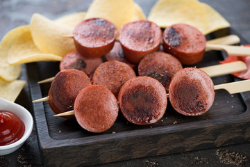 Brochettes with slices of roasted sausages and potato chips, close-up, selective focus