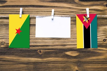 Hanging flags of French Guiana and Mozambique attached to rope with clothes pins with copy space on white note paper on wooden background.Diplomatic relations between countries.