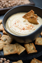 Close-up of crackers with pumpkin seeds and a bowl of freshly made hummus, selective focus, vertical shot