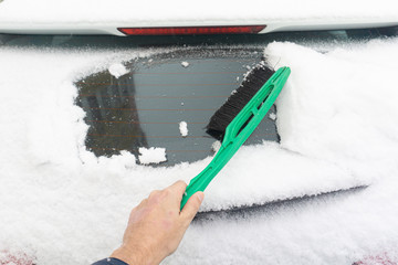 Man cleaning car from snow with brush. Snow-covered car windshield. parked car covered with snow during snowing in winter time.