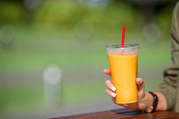 Mango smoothie in a glass in female hand close up