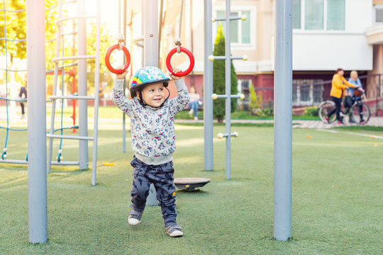 Cute adorable toddler boy enjoy swinging using gymnastic rings at sport playground on residential apartment building outdoors. Happy child playing and doing exercise with equipment outside. Healthy