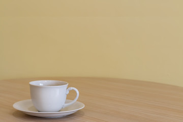 White coffee or tea cup with not soft stream smoke put on wooden table in a living room and blurry dark yellow cement wall with window lighting background. Selective focus and copy space.